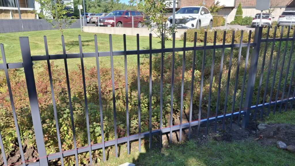 Tummanharmaa metalliaita asennettuna taloyhtiön pihan ja pysäköintialueen väliin